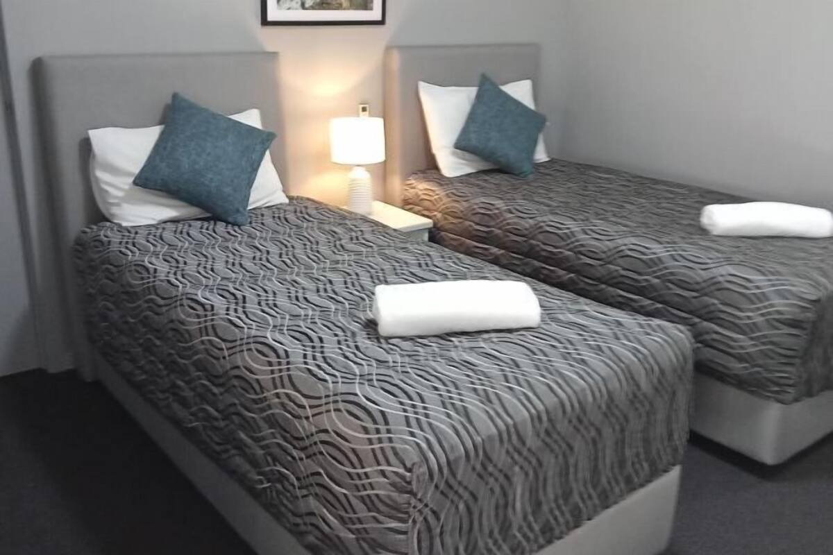 A hotel room with two beds, each with patterned bedding and pillows, a bedside lamp, and a framed picture on the wall.