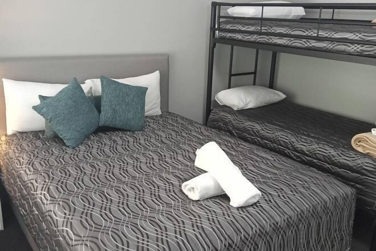 A bunk bed with a patterned bedspread, pillows, and a rolled towel on the lower bunk.