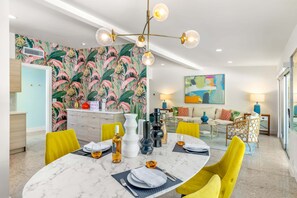 Un espace repas moderne avec une table en marbre, des chaises jaunes et un papier peint aux motifs tropicaux.
