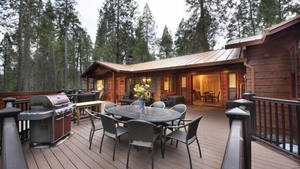 Una terraza de madera con mobiliario exterior, una parrilla y una zona de comedor con mesa y sillas.