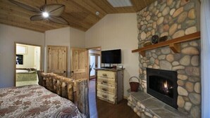 Un dormitorio con chimenea de piedra, techo de madera y cama con colcha estampada.