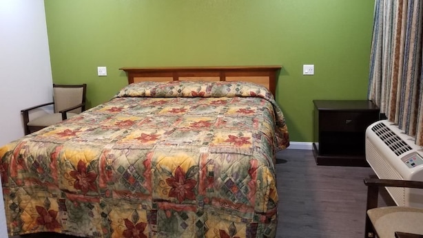 A bedroom with a bed, a chair, a nightstand, and an air conditioning unit. - Travis Lodge Motel 16 (Oakland)