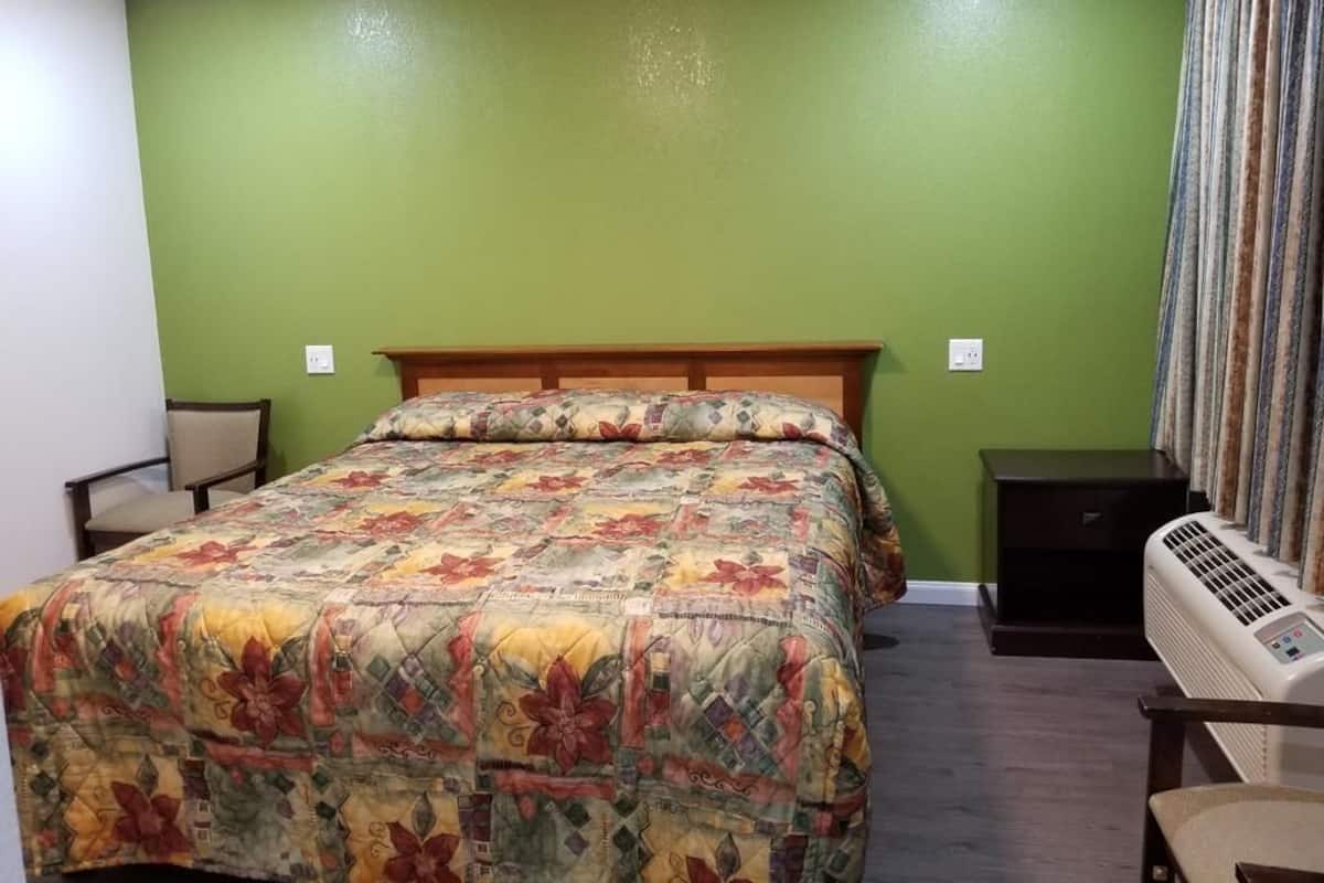 A bedroom with a bed, a chair, a nightstand, and an air conditioning unit.