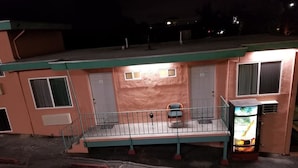 A motel with a balcony, a small outdoor seating area, and a neon sign. - Travis Lodge Motel 16 (Oakland)