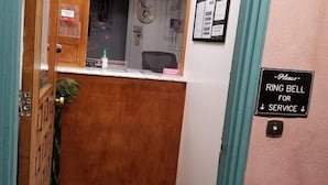 A reception area with a wooden counter, a black mat, a sign for the ring bell, and a bulletin board. - Travis Lodge Motel 16 (Oakland)