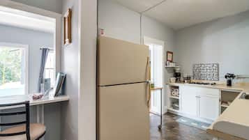A compact kitchen with a refrigerator, a dining area with a chair, and a window with curtains.