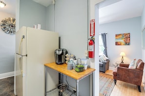 Een praktische keuken met een koelkast, koffieapparaat en een tafeltje met een waterkoker en kopjes.