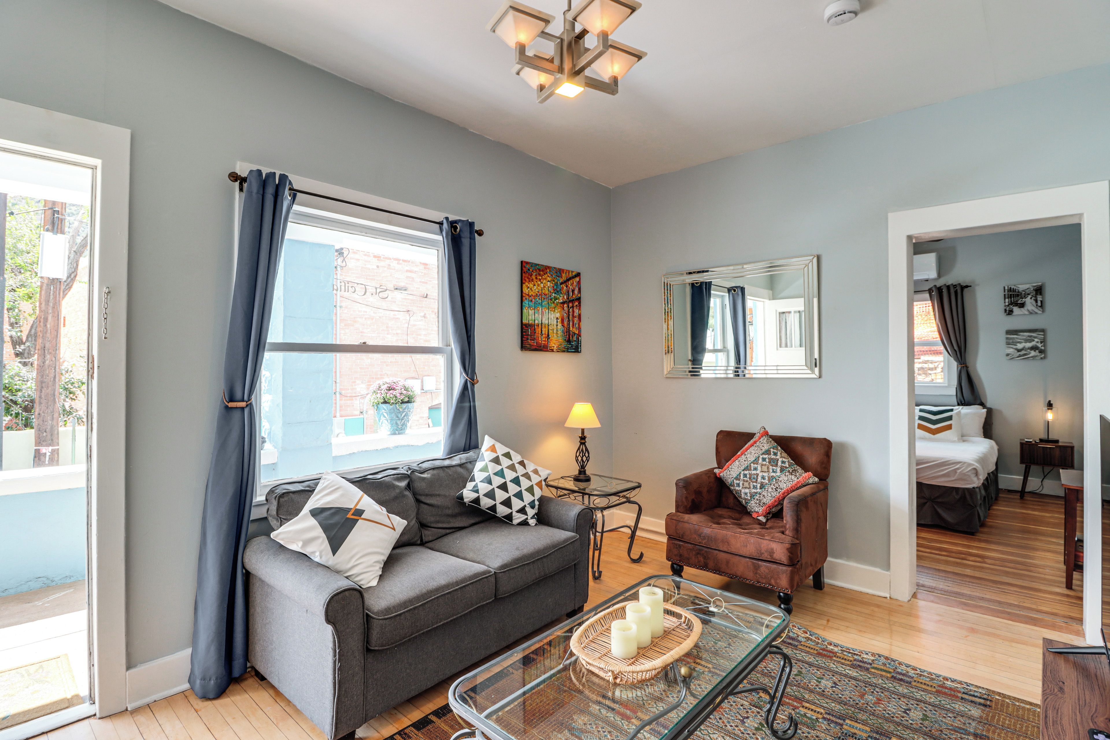 A living room with a grey sofa, a brown armchair, a glass coffee table, and a patterned rug.