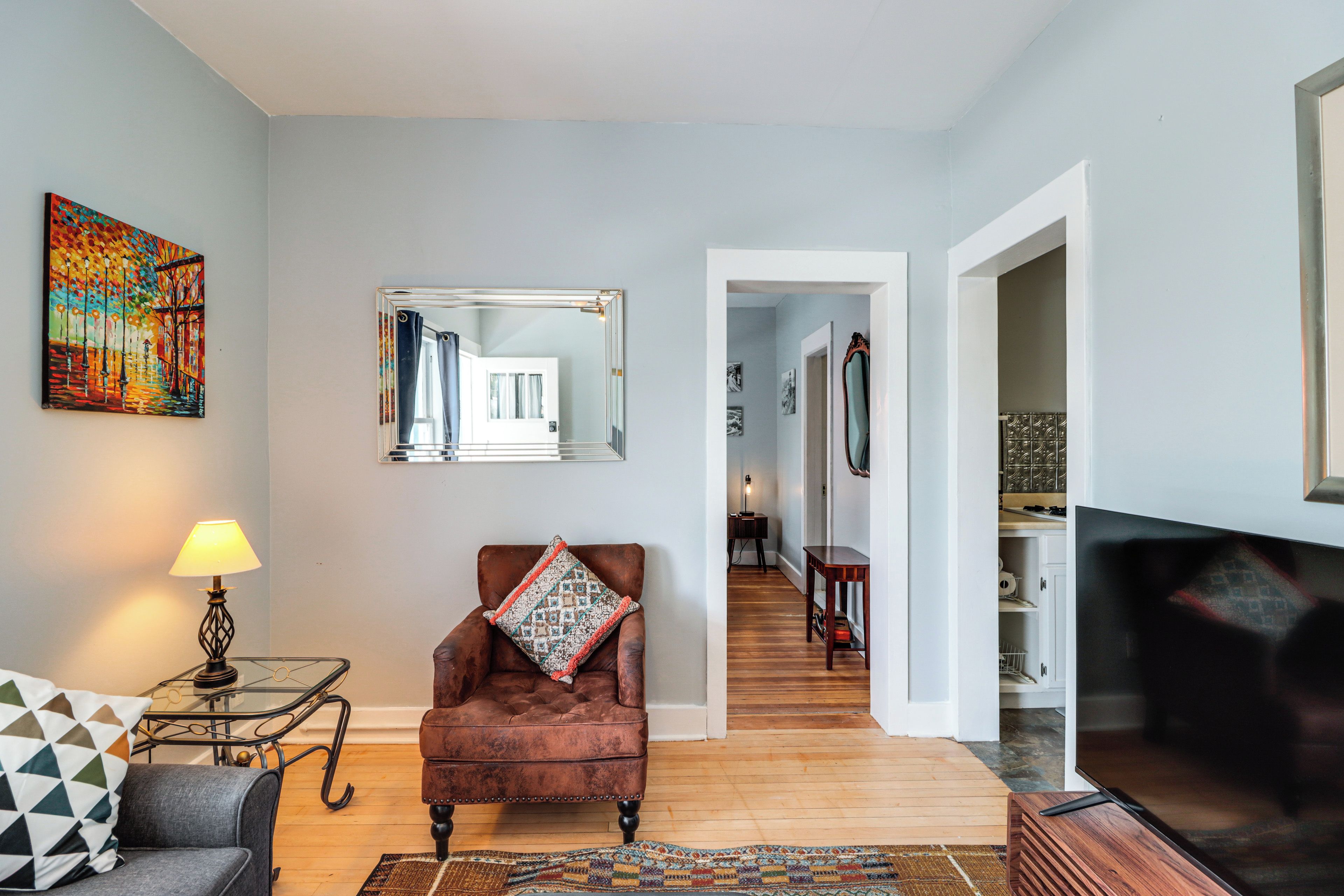 A living room with a brown leather armchair, a glass coffee table, a lamp, and a colorful painting on the wall.