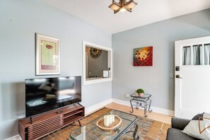 A living room with a flat-screen TV, a framed artwork, a decorative mirror, and a door with curtains. - 'St Ceilia' Apt - Walk to Bisbee Attractions! (Bisbee)