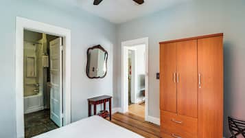 A bedroom with a bed, a wooden wardrobe, a mirror, and a door leading to a bathroom.