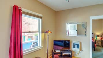 A living room with a TV, a floor lamp, a window with red curtains, a mirror, and a radiator.