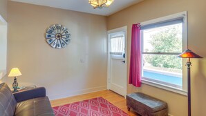 A room with a clock on the wall, a sofa, a bench, a lamp, and a window with curtains. - 'St Ceilia' Apt - Walk to Bisbee Attractions! (Bisbee)