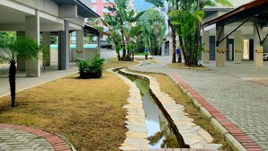 Une cour intérieure urbaine moderne, dotée d’une allée pavée, d’un petit élément décoratif aquatique et d’une végétation luxuriante tout autour.