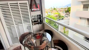 Un balcon doté d’une table en verre et de chaises en osier, offrant une vue sur un quartier résidentiel avec ses maisons et sa verdure.