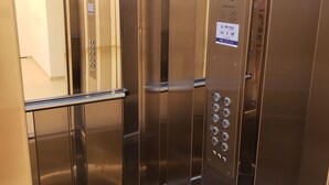 L’intérieur d’un ascenseur, avec des parois métalliques, un panneau de commande doté de boutons et une barre d’appui.