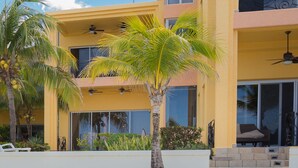 A yellow two-story building with balconies, palm trees, and a clear blue sky. - Beachfront Luxury at Coral Sands (Roatan)