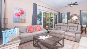 A spacious living room with a grey sofa, a recliner, a coffee table, and a large window with curtains. - Beachfront Luxury at Coral Sands (Roatan)