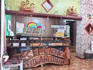 A reception desk with a wooden design, a sign for 'RECEPTION,' and various informational posters.