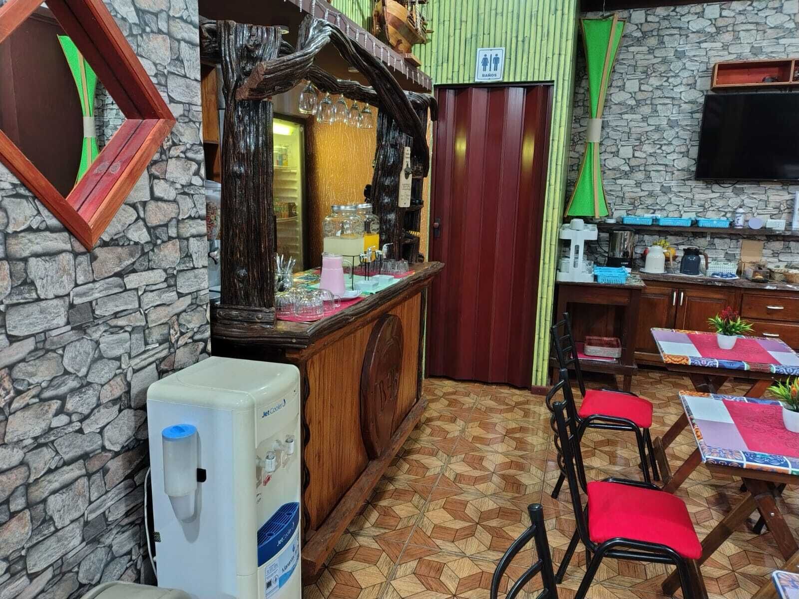 A room with a stone wall, a wooden counter with a mirror, a JetCode water dispenser, and a TV mounted on the wall.