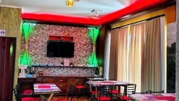 A restaurant with a stone wall, a flat-screen TV, and tables with red chairs.
