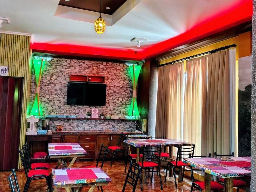 A restaurant with a stone wall, a flat-screen TV, and tables with red chairs.