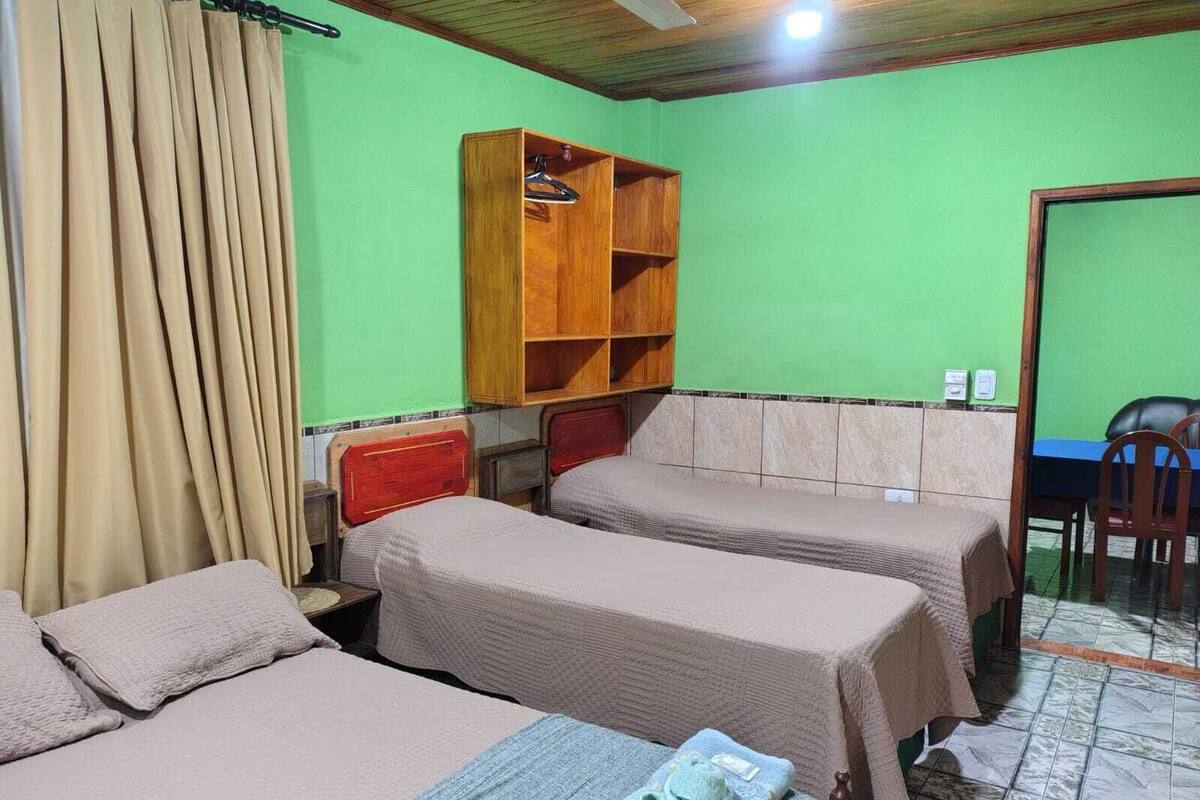 Quarto com duas camas, uma prateleira de madeira, uma cadeira e uma mesa.