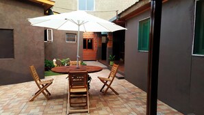 A patio with a round table and four chairs, an umbrella, and a small garden area. - Arcoíris Residencial (Puerto Iguazú)