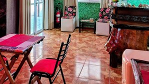 A room with a green textured wall, a red and white striped sign, a window with curtains, a table with a red chair, and a piano. - Arcoíris Residencial (Puerto Iguazú)