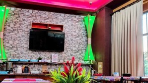 A restaurant with a stone wall, a flat-screen TV, a potted plant, and a table with a colorful table runner. - Arcoíris Residencial (Puerto Iguazú)