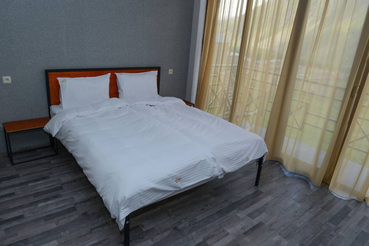 A neatly made bed with white bedding and a wooden headboard in a room with grey walls and a wooden floor.