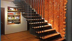 Una scala con finitura in legno e ringhiere in metallo che conduce a una stanza con parete in mattoni e una lampada a sospensione.