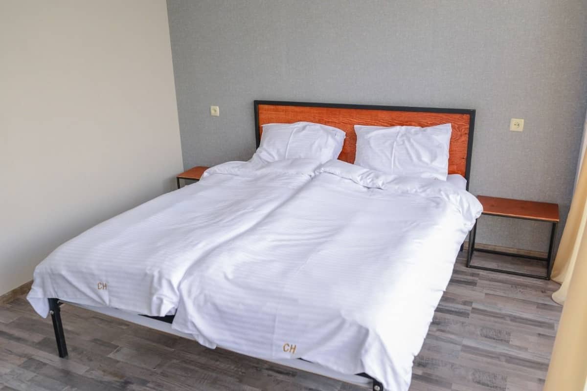 A neatly made bed with white linens and a wooden headboard, a bedside table, and a bench against the wall.