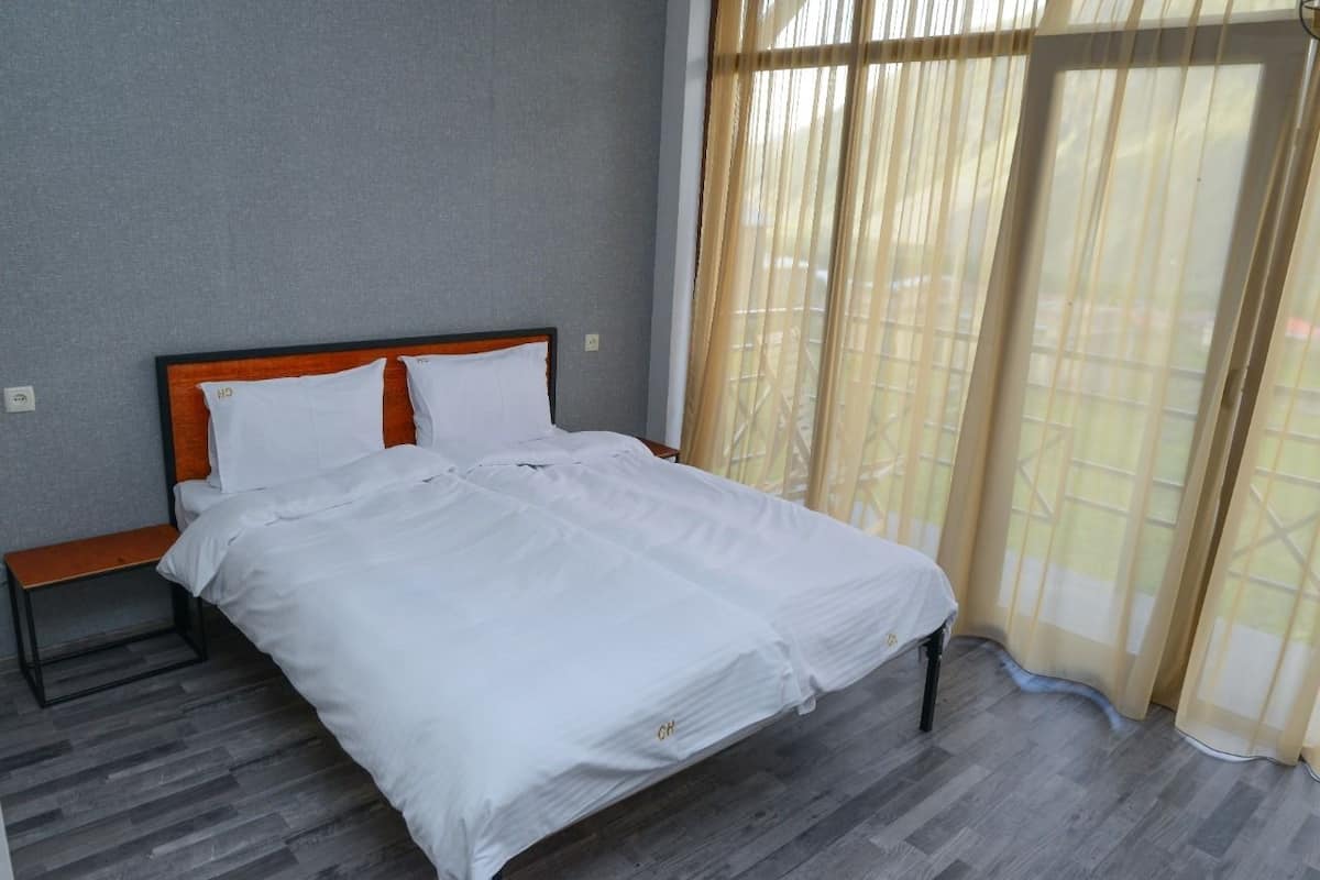 A neatly made bed with white linens in a room with grey walls and a wooden headboard.