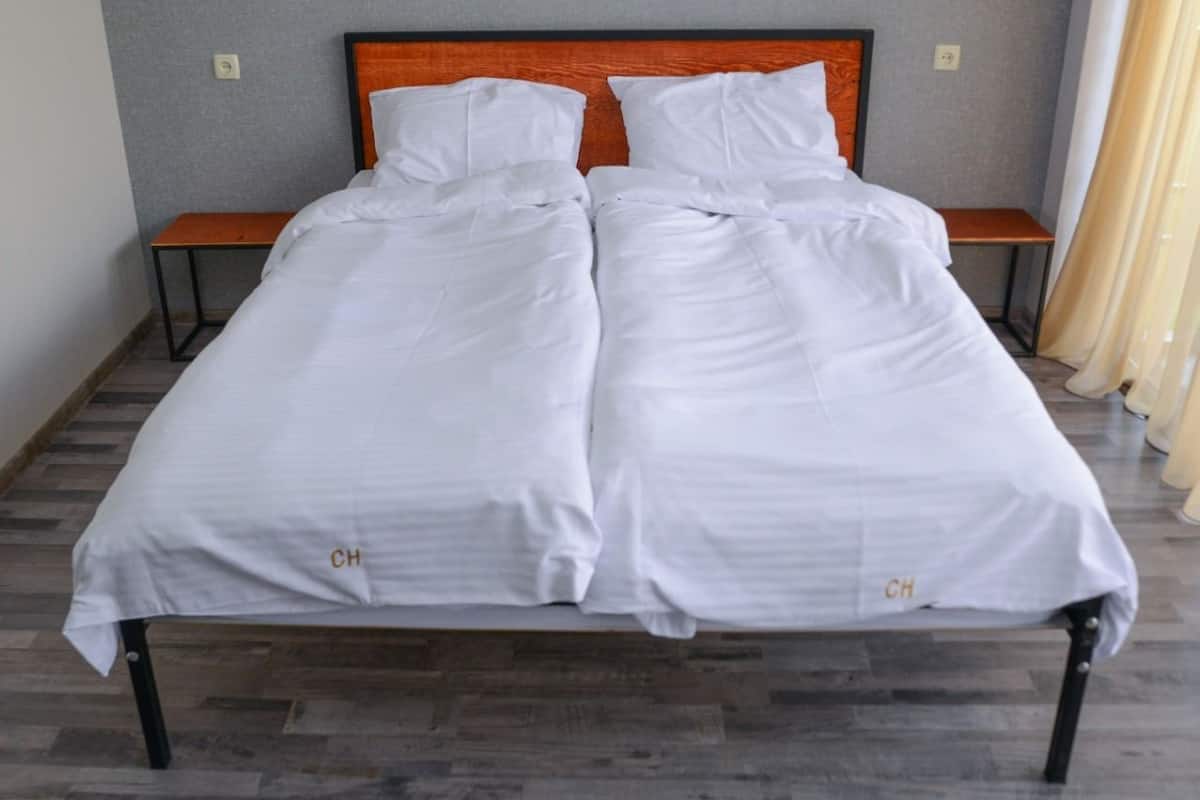 A double bed with white bedding and a wooden headboard. There are two bedside tables and a small bench.