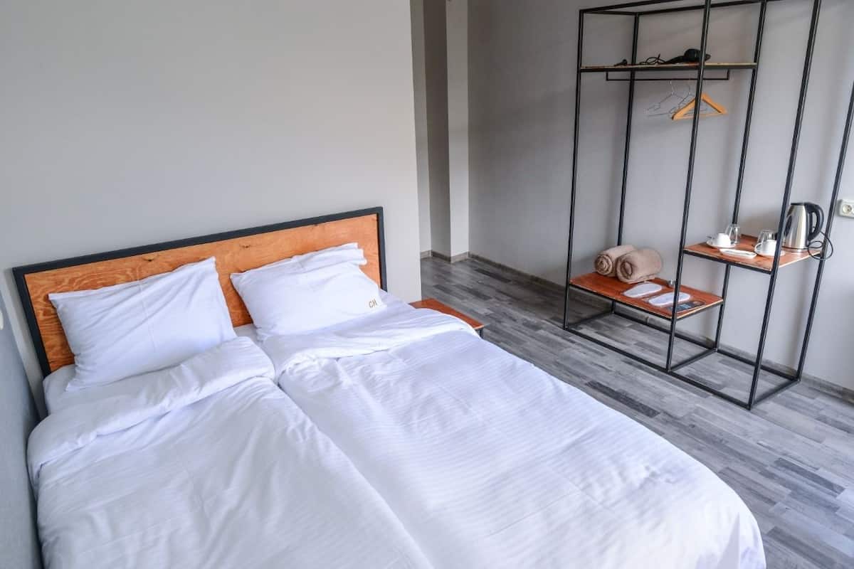 A neatly made bed with white linens and a wooden headboard. Adjacent to the bed is a metal wardrobe with shelves and a hanging rack.