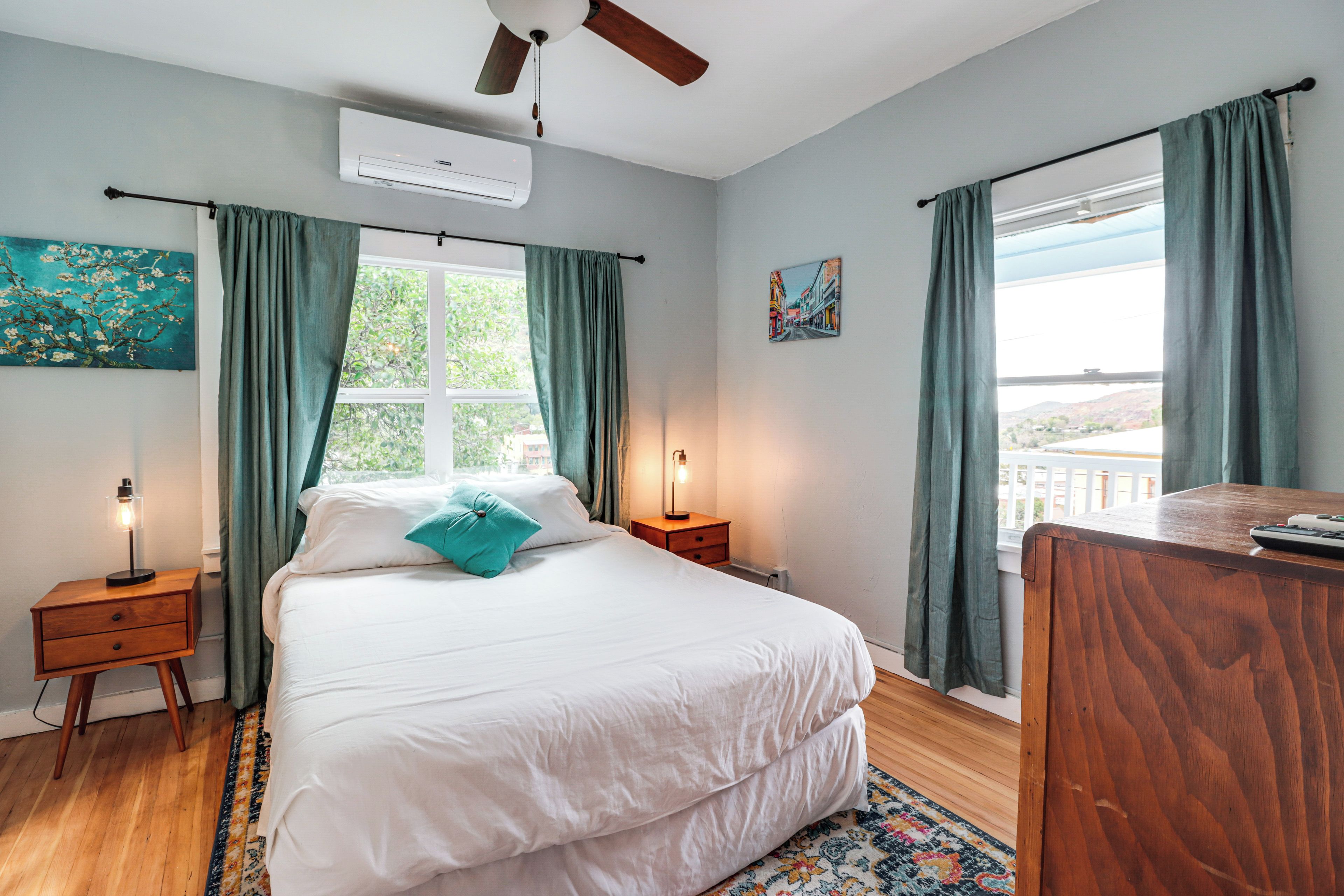 A bedroom with a bed, a nightstand, a lamp, a ceiling fan, an air conditioner, and a window with curtains.