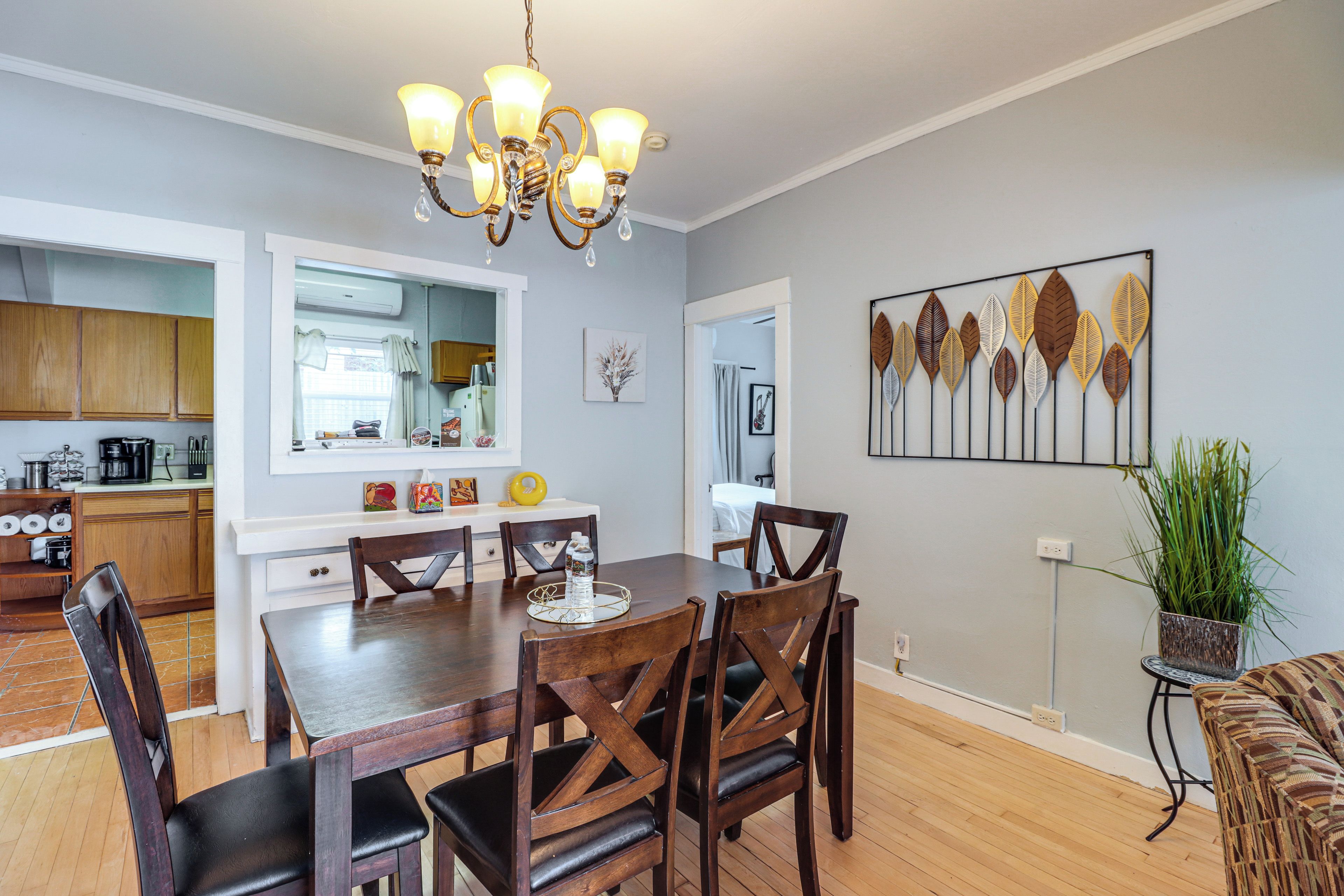 A dining area with a wooden table and chairs, a chandelier, and a wall-mounted artwork.