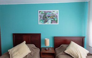 A room with teal walls, two wooden beds with matching headboards, a bedside table with a lamp, and a framed picture of a bird on a branch. - Apartments Cumbaya Quito Ec (Cumbayá)