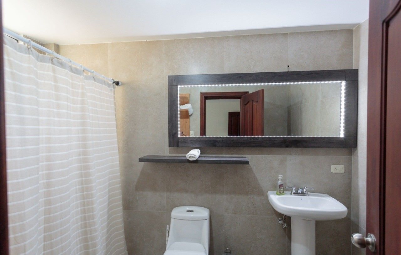 Ein Badezimmer mit Duschvorhang, Toilette, Waschbecken und einem beleuchteten Spiegel.