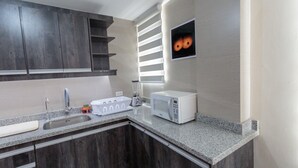 A modern kitchen with dark wooden cabinets, a granite countertop, a built-in microwave, and a window with blinds. - Apartments Cumbaya Quito Ec (Cumbayá)