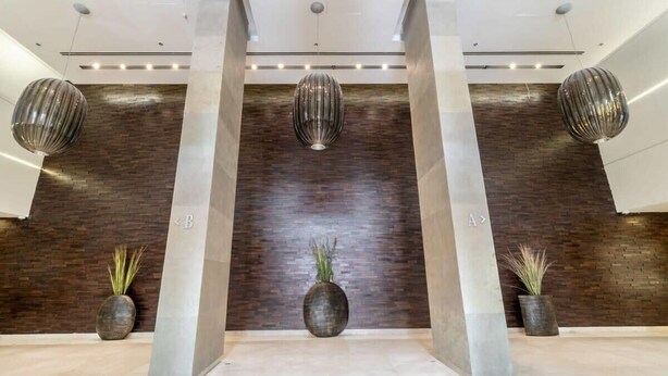 A modern lobby with a dark wood wall, two large columns, and three spherical light fixtures.