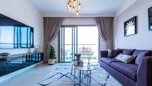 A modern living room with a sofa, a coffee table, and a TV. There is a balcony with a view of the city.