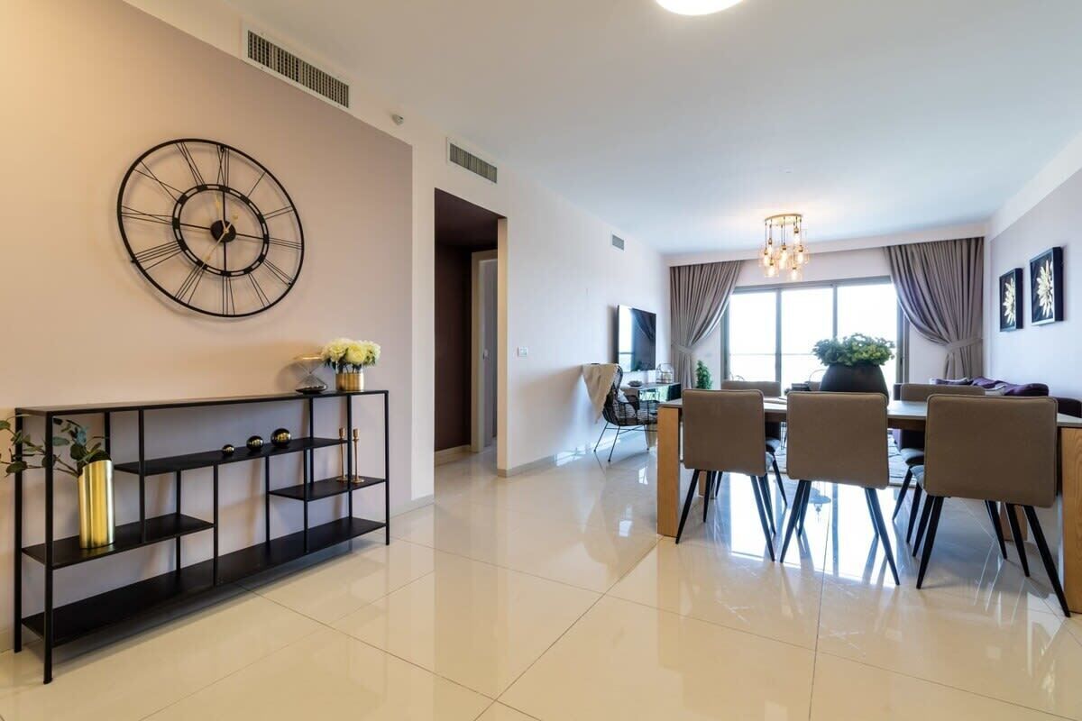 Un salon moderne avec un coin repas, comprenant une console noire, une grande horloge murale et une table à manger avec des chaises.