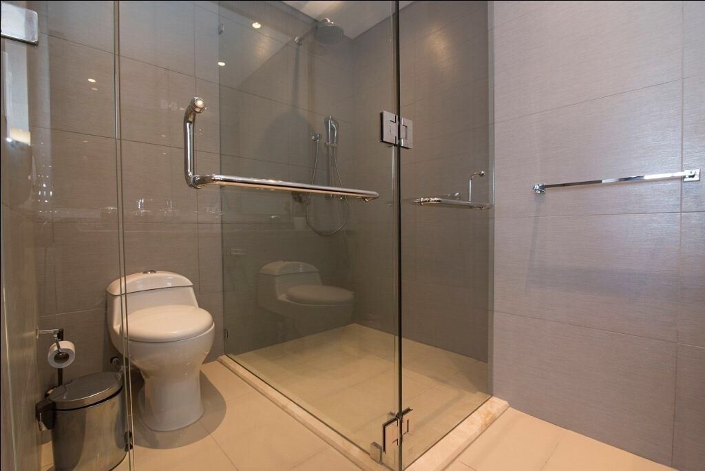 A modern bathroom with a glass-enclosed shower, a toilet, and a trash bin.