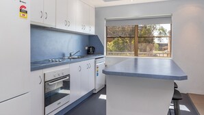 A modern kitchen with white cabinets, a built-in oven, a coffee maker, and a large window providing a view of trees and buildings. - Two Storey Apartment Sandcastle 7 (Tuncurry)