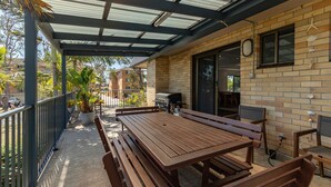A covered patio with a wooden table and benches, a barbecue grill, and a brick wall with decorative shells. - Two Storey Apartment Sandcastle 7 (Tuncurry)