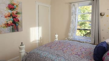 Un dormitorio con una colcha estampada, una ventana con cortinas, una puerta blanca y un adorno de estrella montado en la pared.