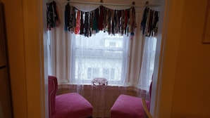Una habitación con un ventanal grande, dos sillas rosas y un perchero colgante.
