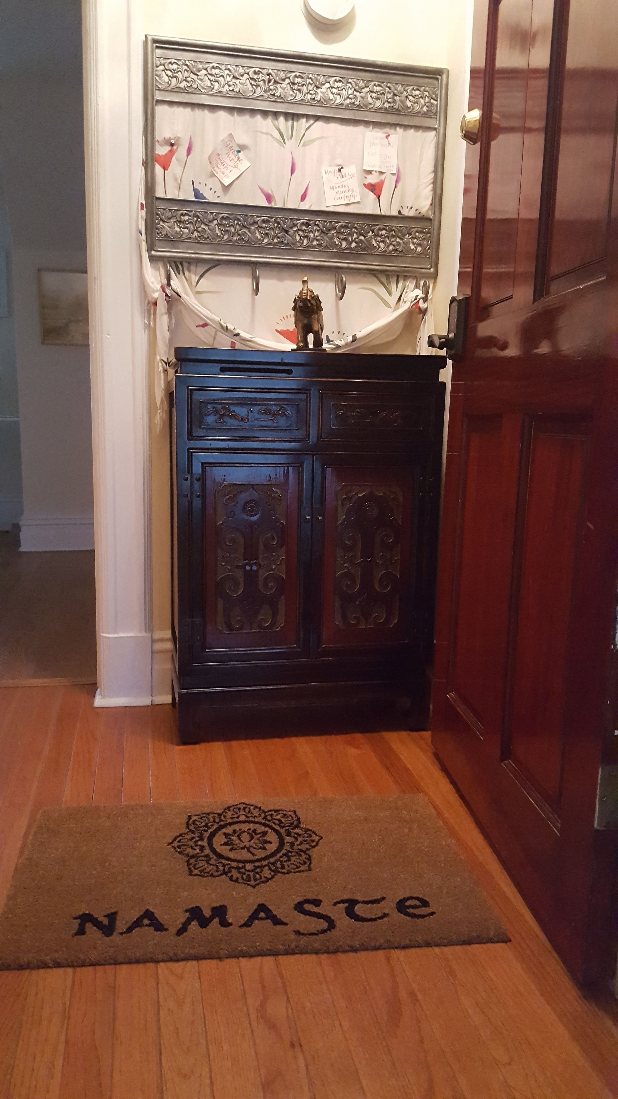 A wooden door with a brass handle, a dark blue cabinet with ornate carvings, and a doormat with the word "NAMASTE" on it.
